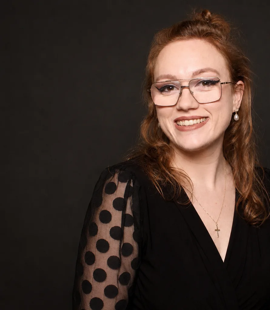 Allie Moore, MC/DJ Allie of Sound of Harmony, smiling in a black dress against a dark studio backdrop, professional wedding MC, DJ and stand-up comedian in Niagara, Ontario
